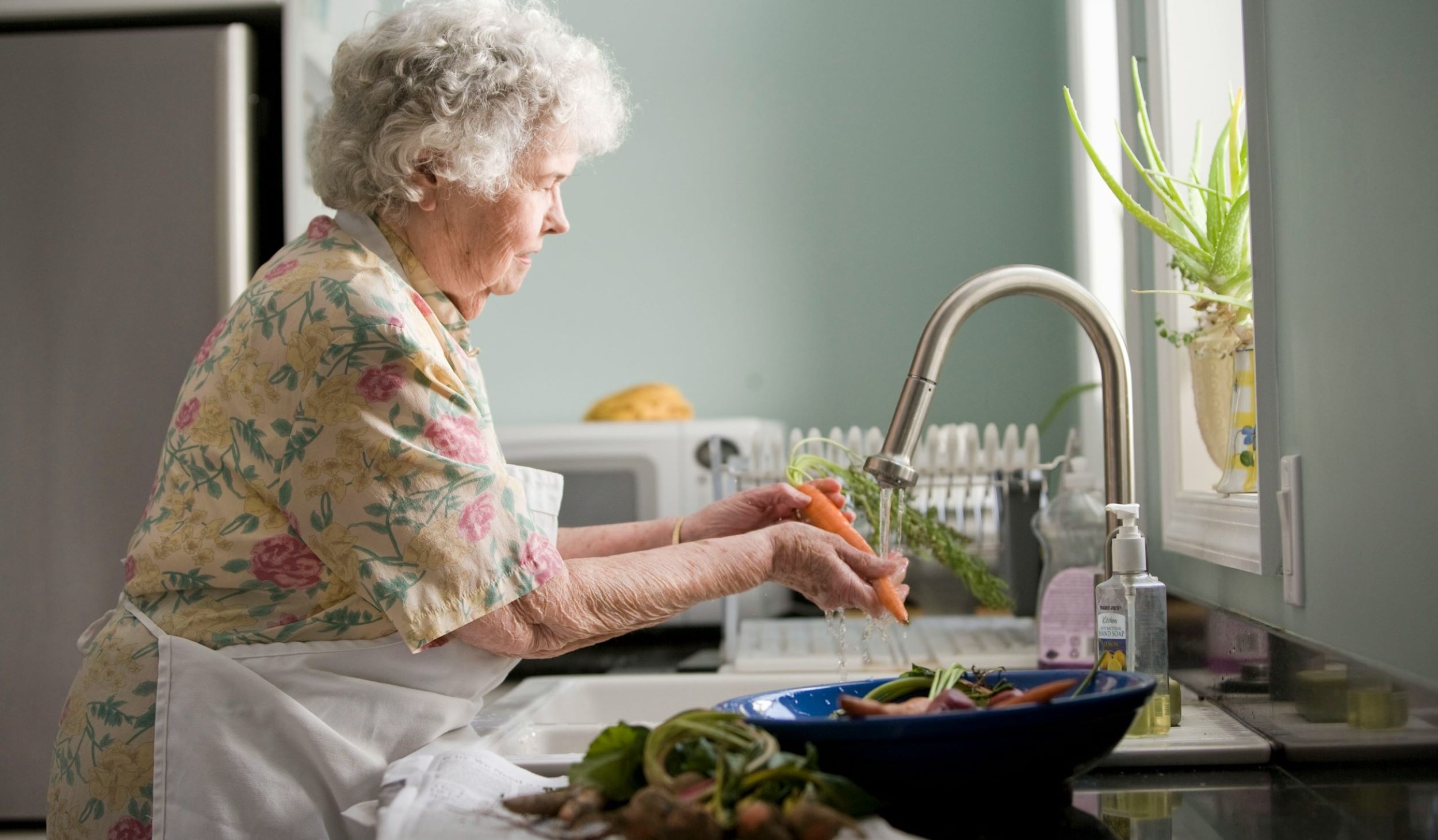 An elderly woman cooks in a kitchen.
