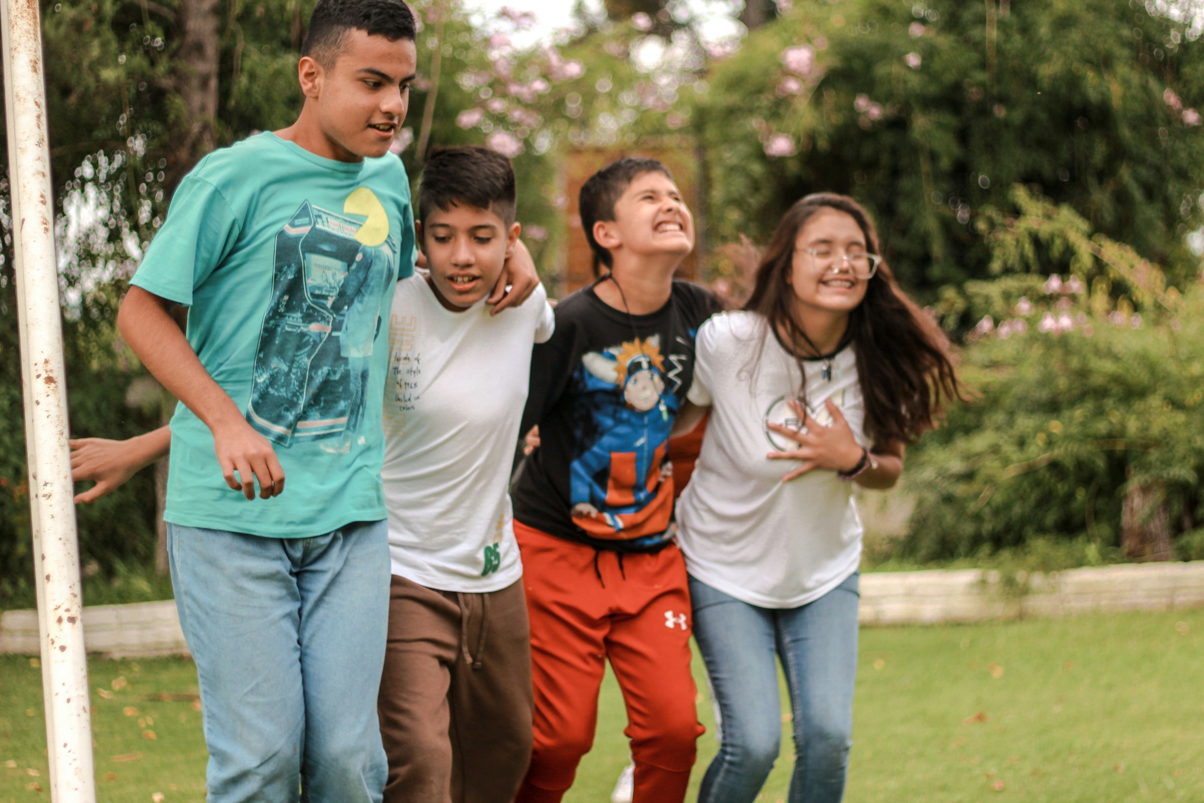 Kids stand together and smile in front of a cluster of trees.