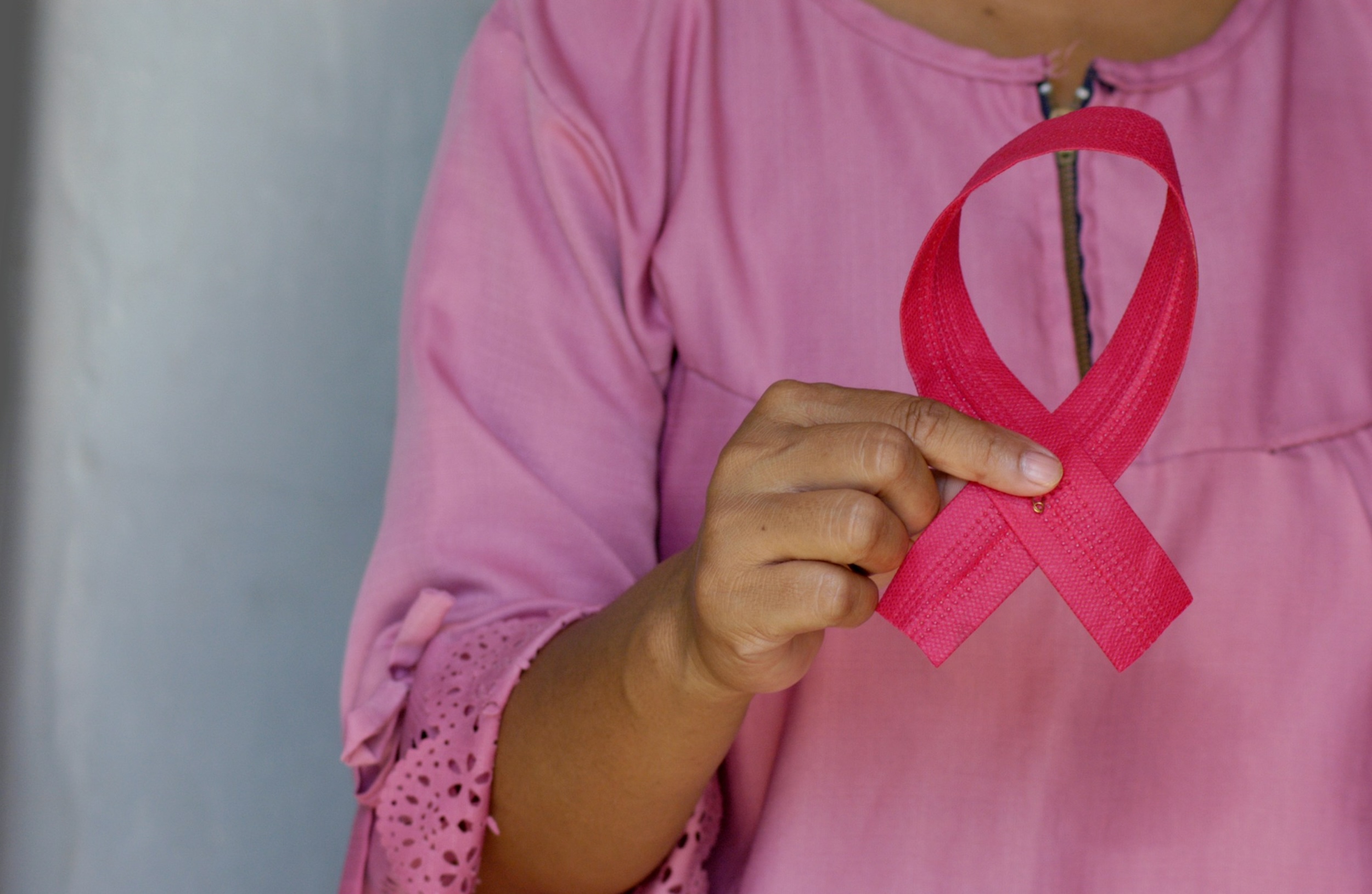 A woman in a pink shirt holds a matching ribbon close to her heart.