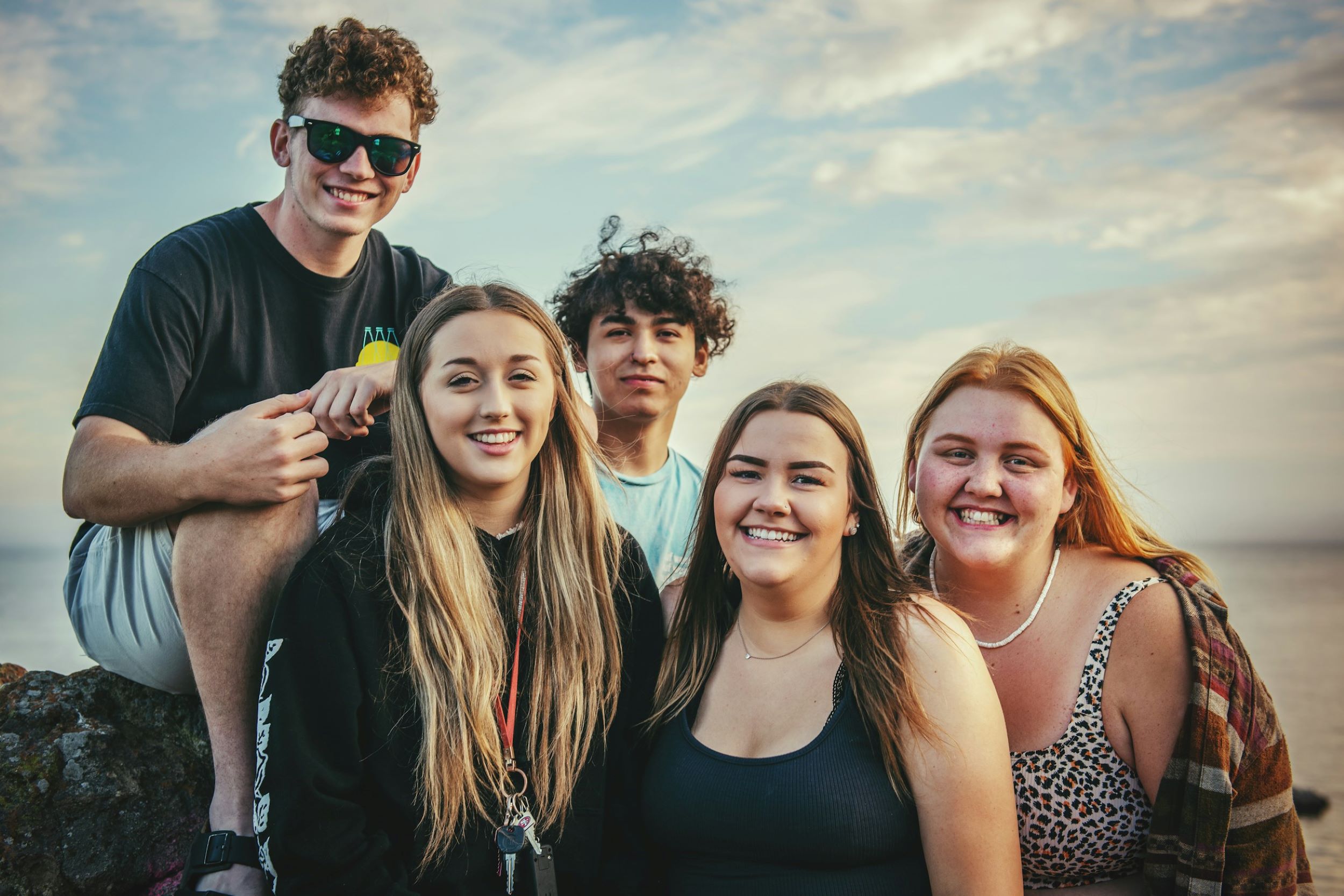 A group of teens smile and pose in front of a beach.