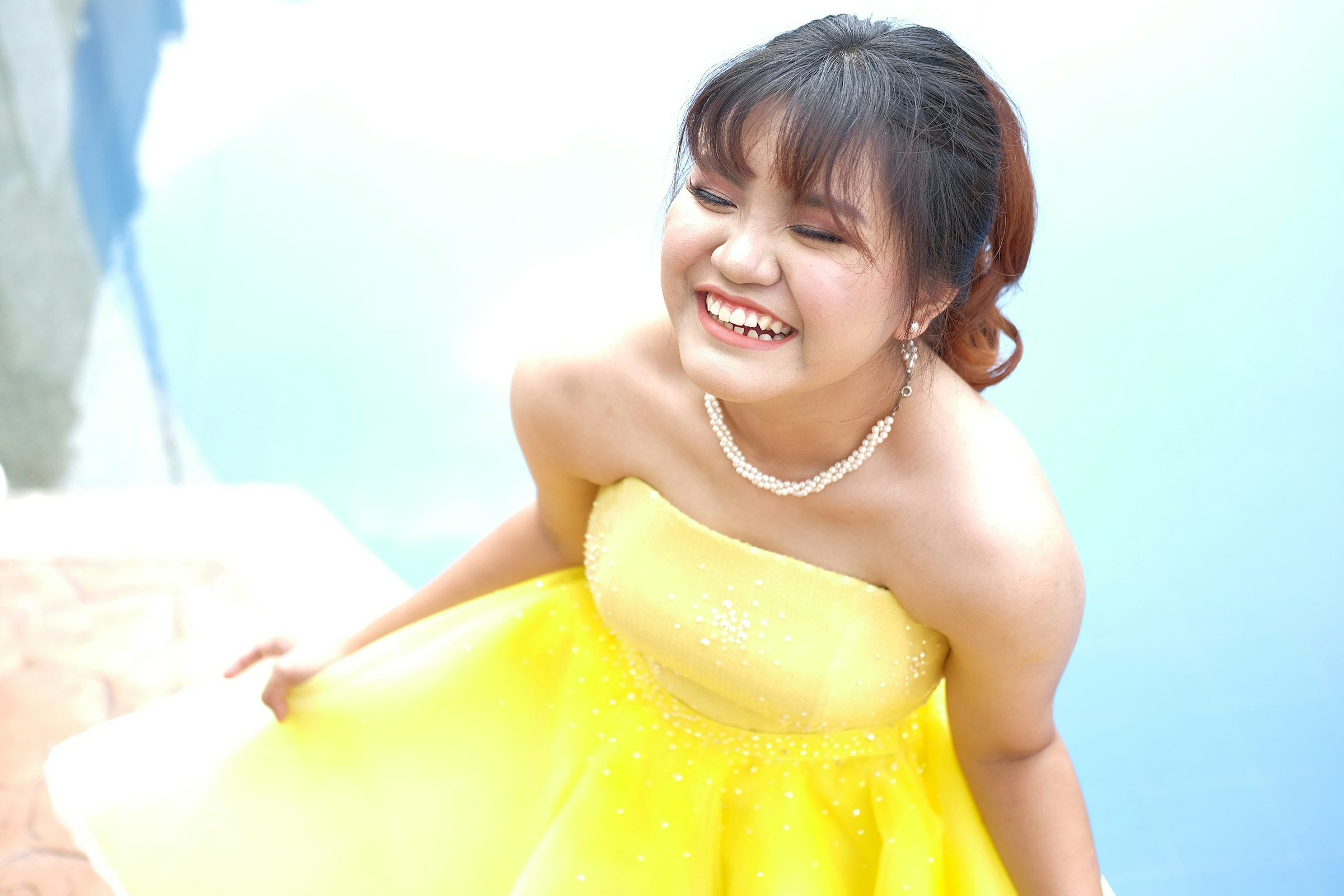 A young woman wears a yellow dress and smiles with her eyes closed.