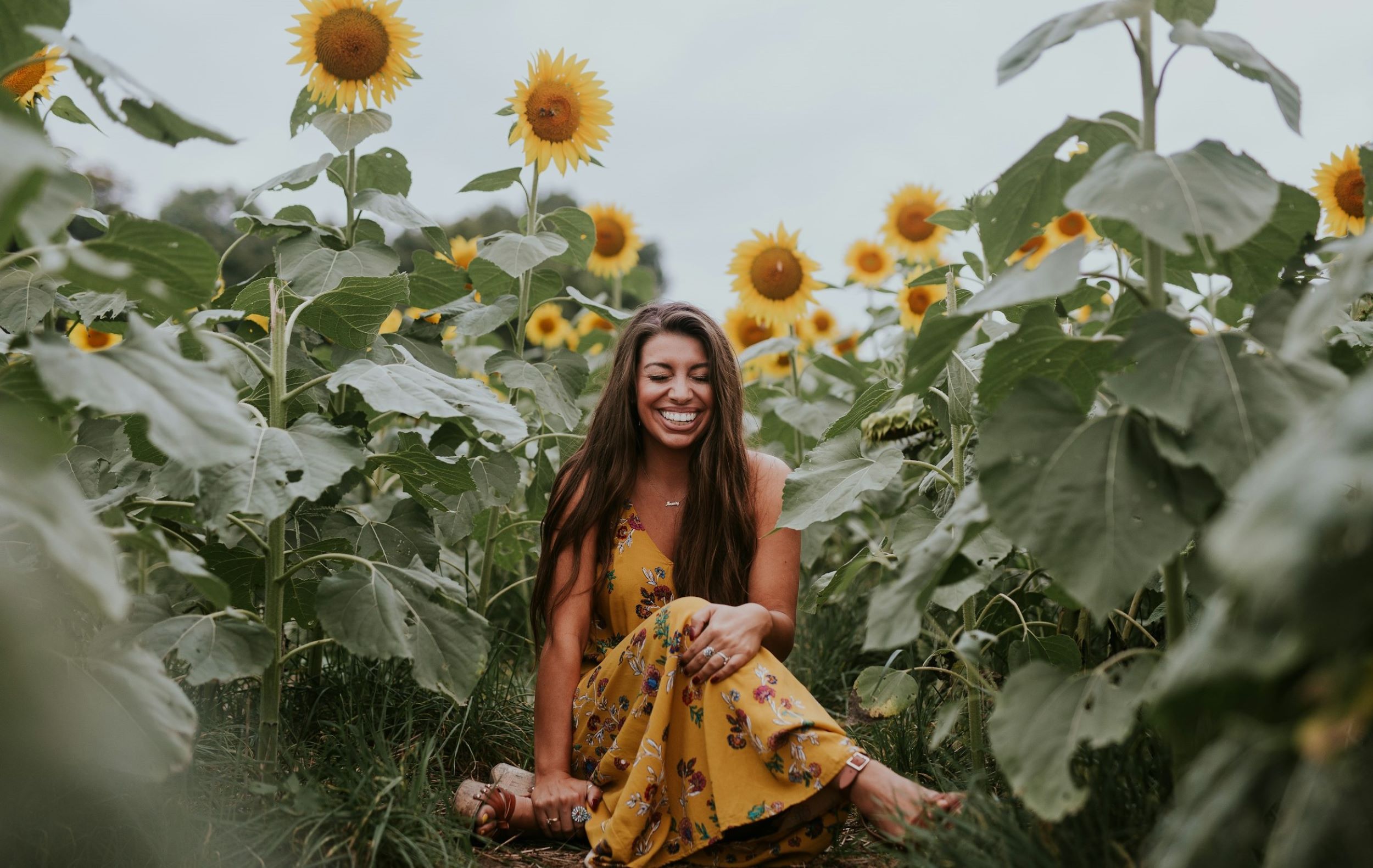 A woman smiles while sitting in a sunflower field.