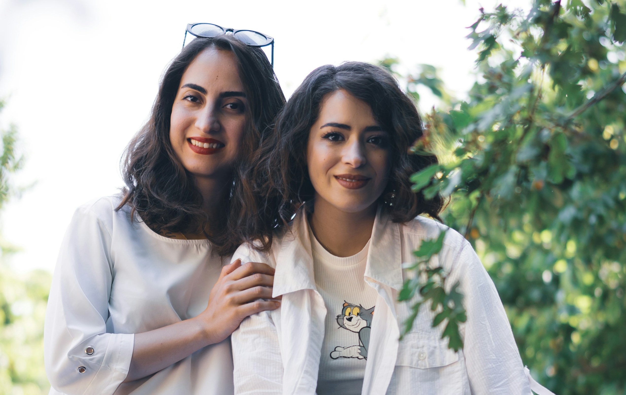 Two women smile and hold hands near a tree.