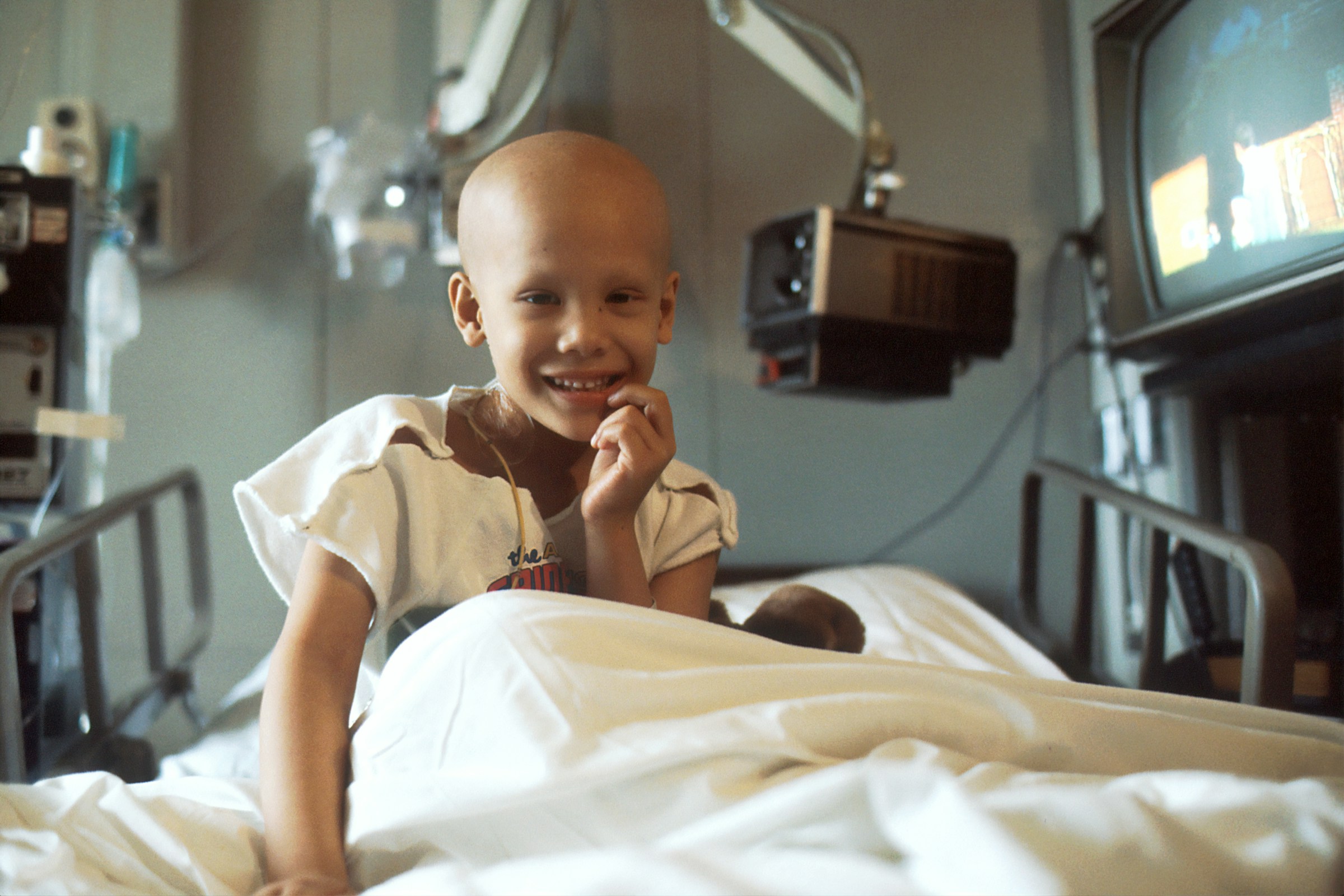 A young cancer patient sits in her hospital bed and smiles.