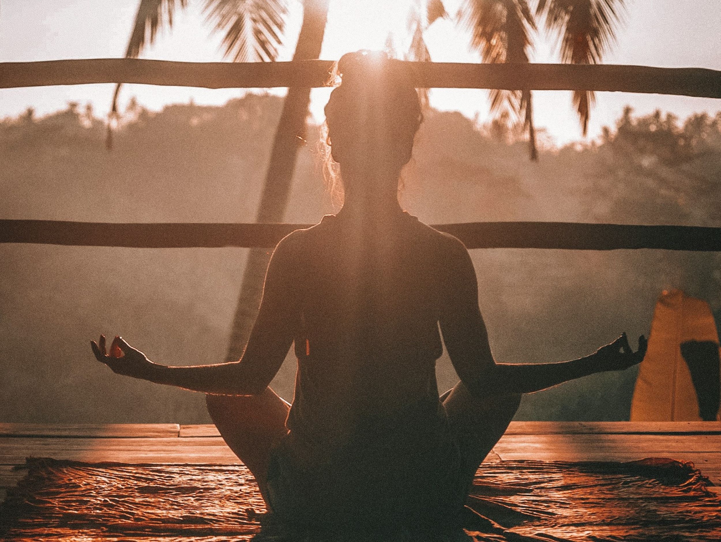 A woman practices meditation outside, bathed in the warm glow of sunset.