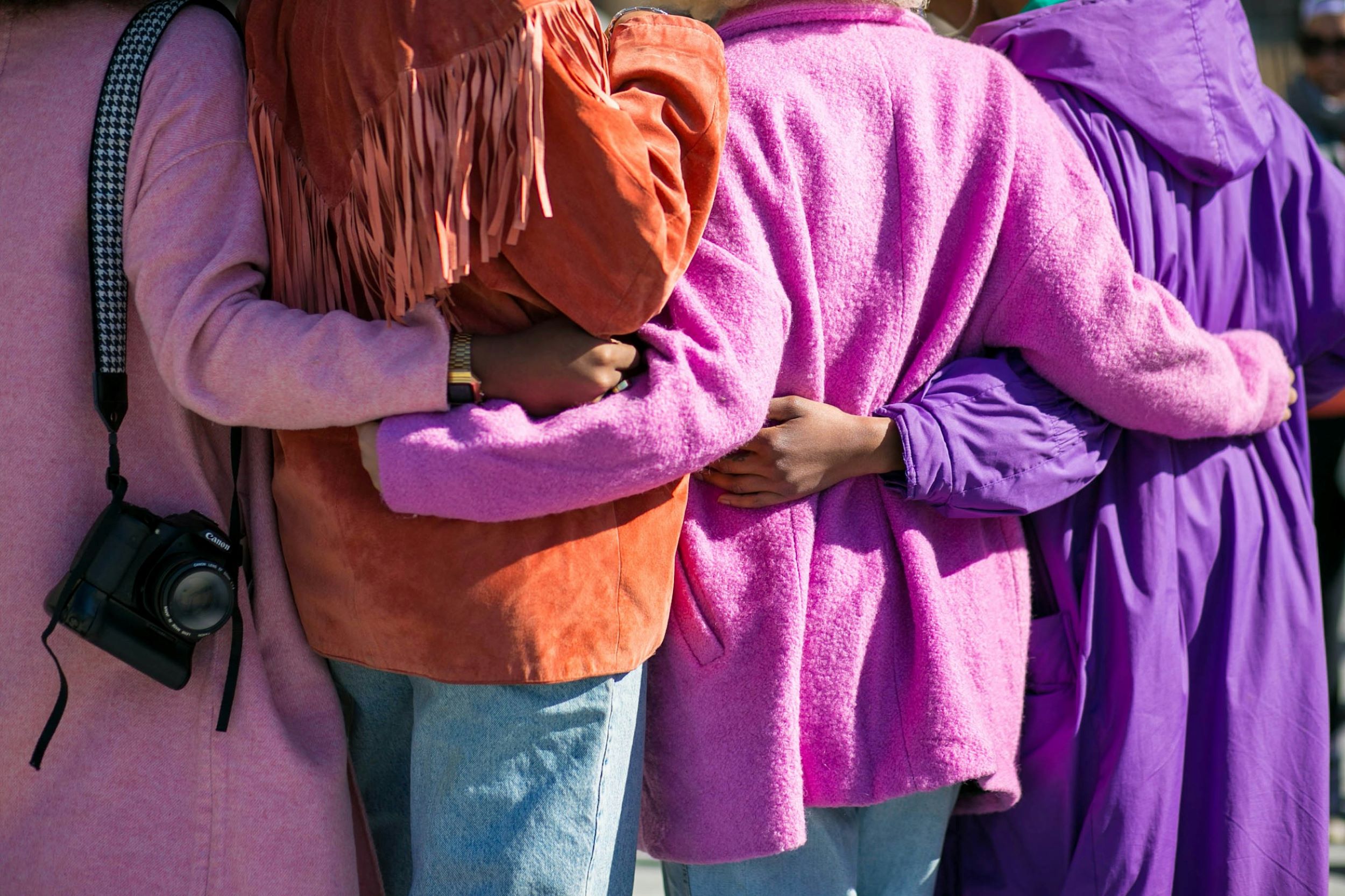 Women with purple and brown jackets huddle together and embrace.