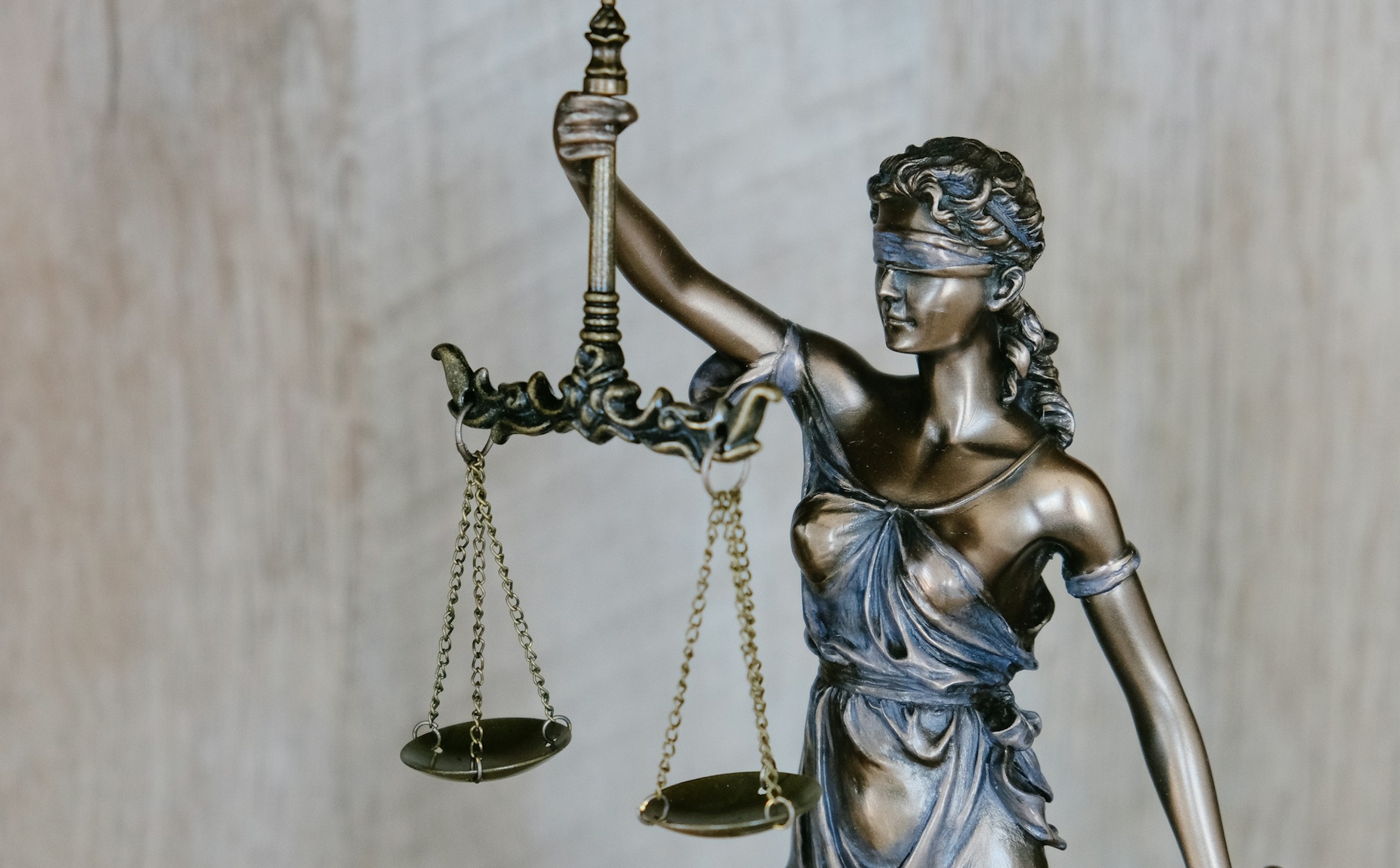 A sculpture of Lady Justice is positioned in front of a textured backdrop.