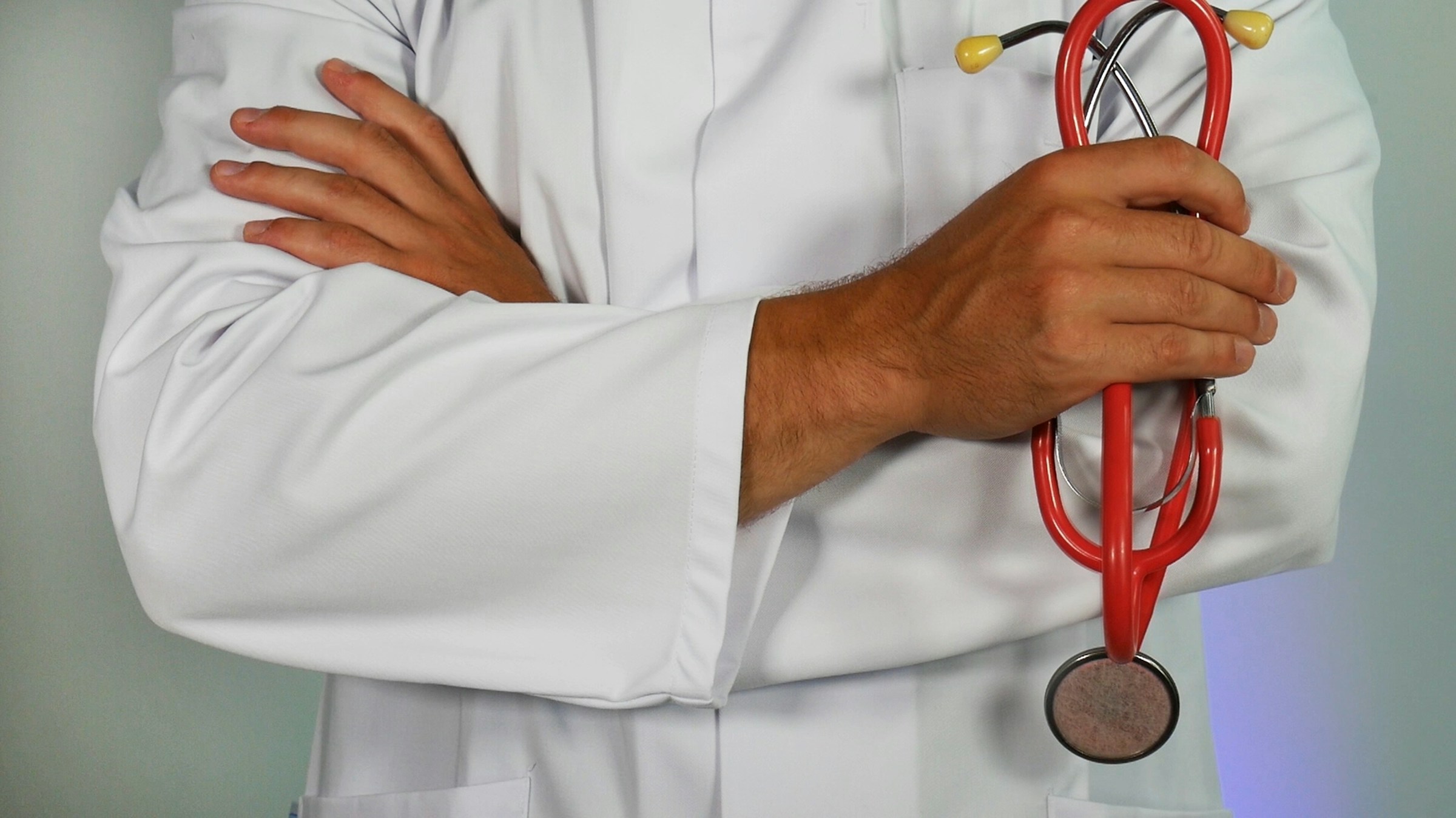 A doctor, dressed in a white coat, crosses his arms against a white background.
