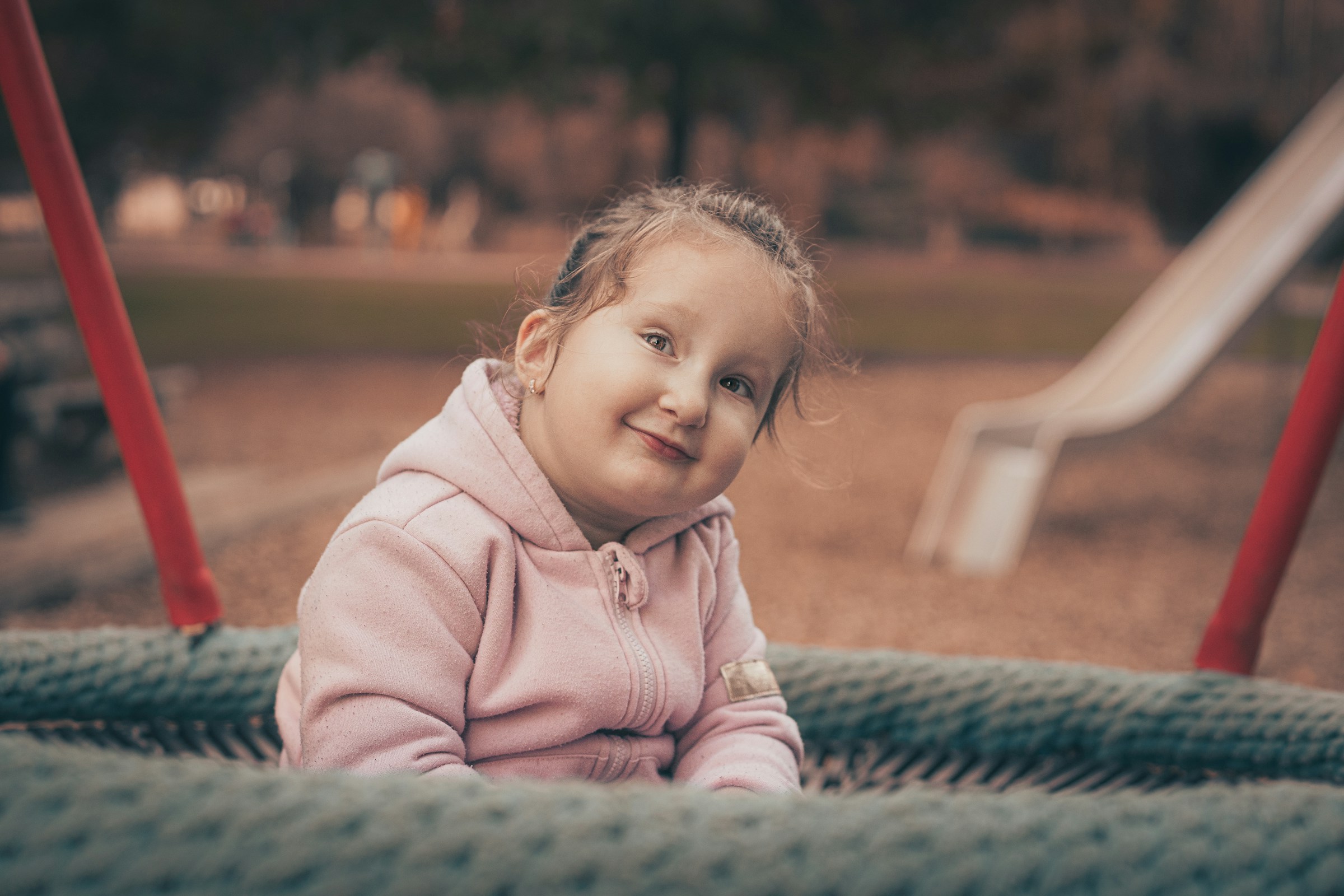 A child with a disability smiles while sitting in a playground.