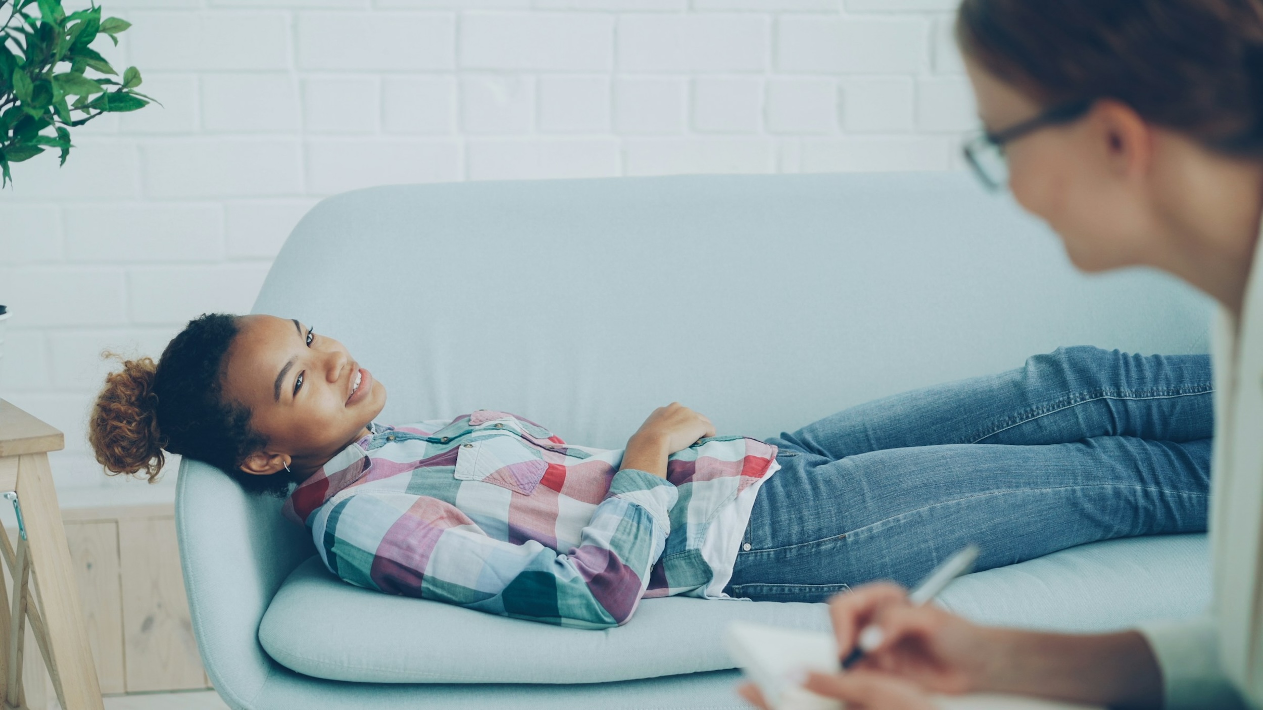 A therapist talks with her patient while jotting notes on a notepad.