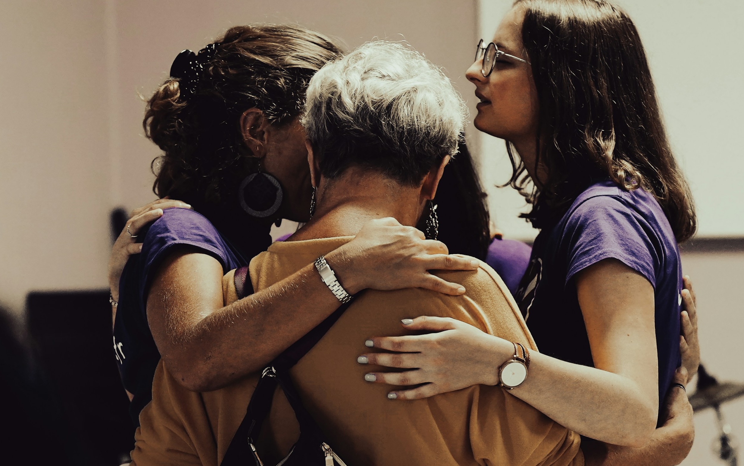 Three women form a circle and embrace.