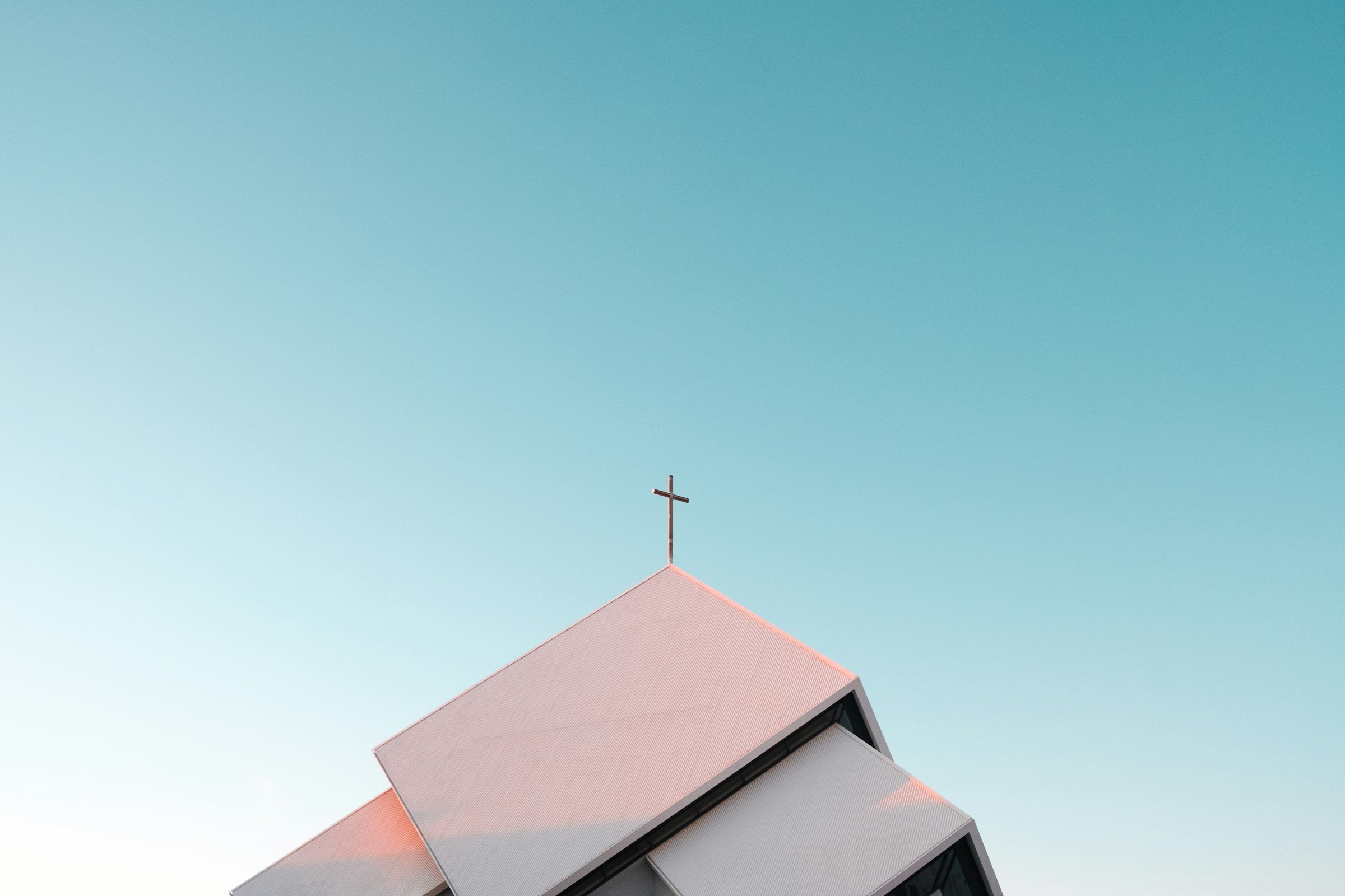 A cross crowns the roof of a white church, gleaming under the bright sunshine.
