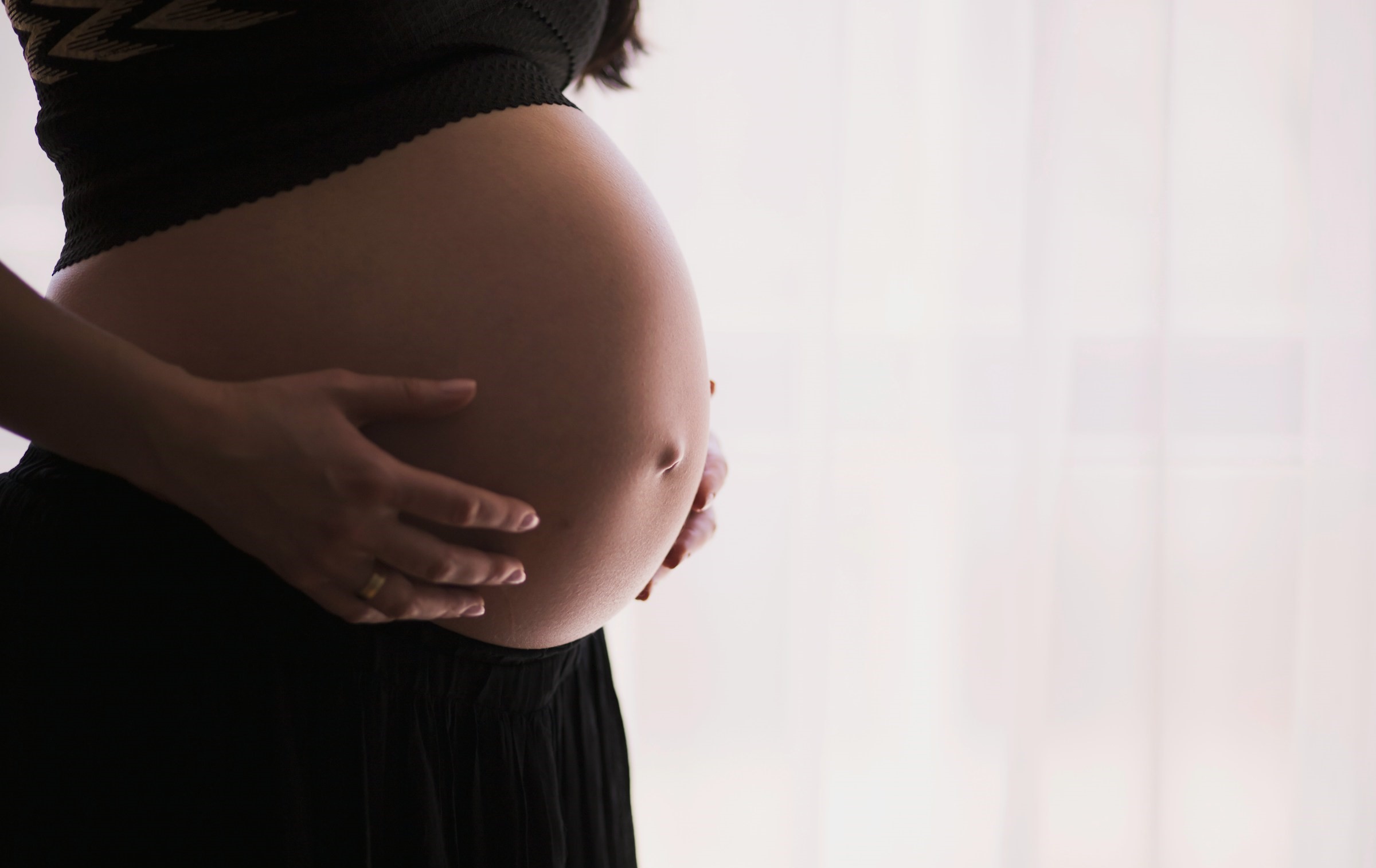 A pregnant woman clutches her belly in front of a white backdrop.