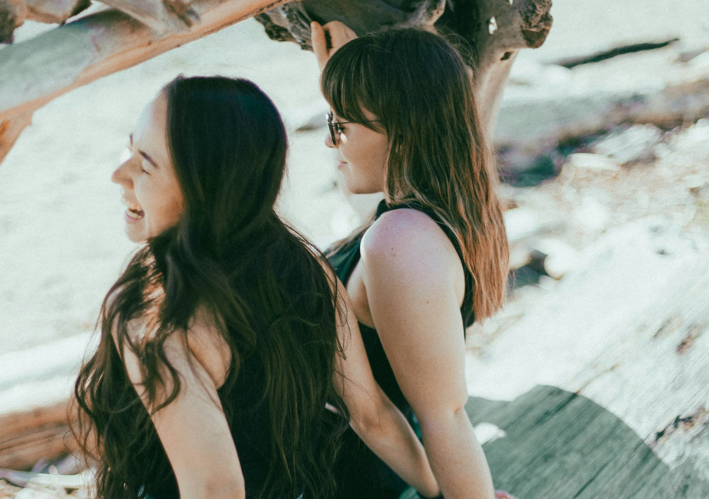 Two women beam with joy as they soak up the sunshine on a sandy beach.