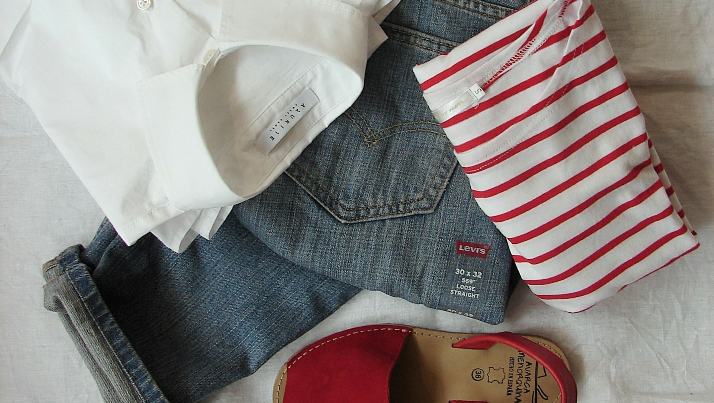 A pair of blue jeans and a striped shirt rest neatly atop a crisp white sheet.