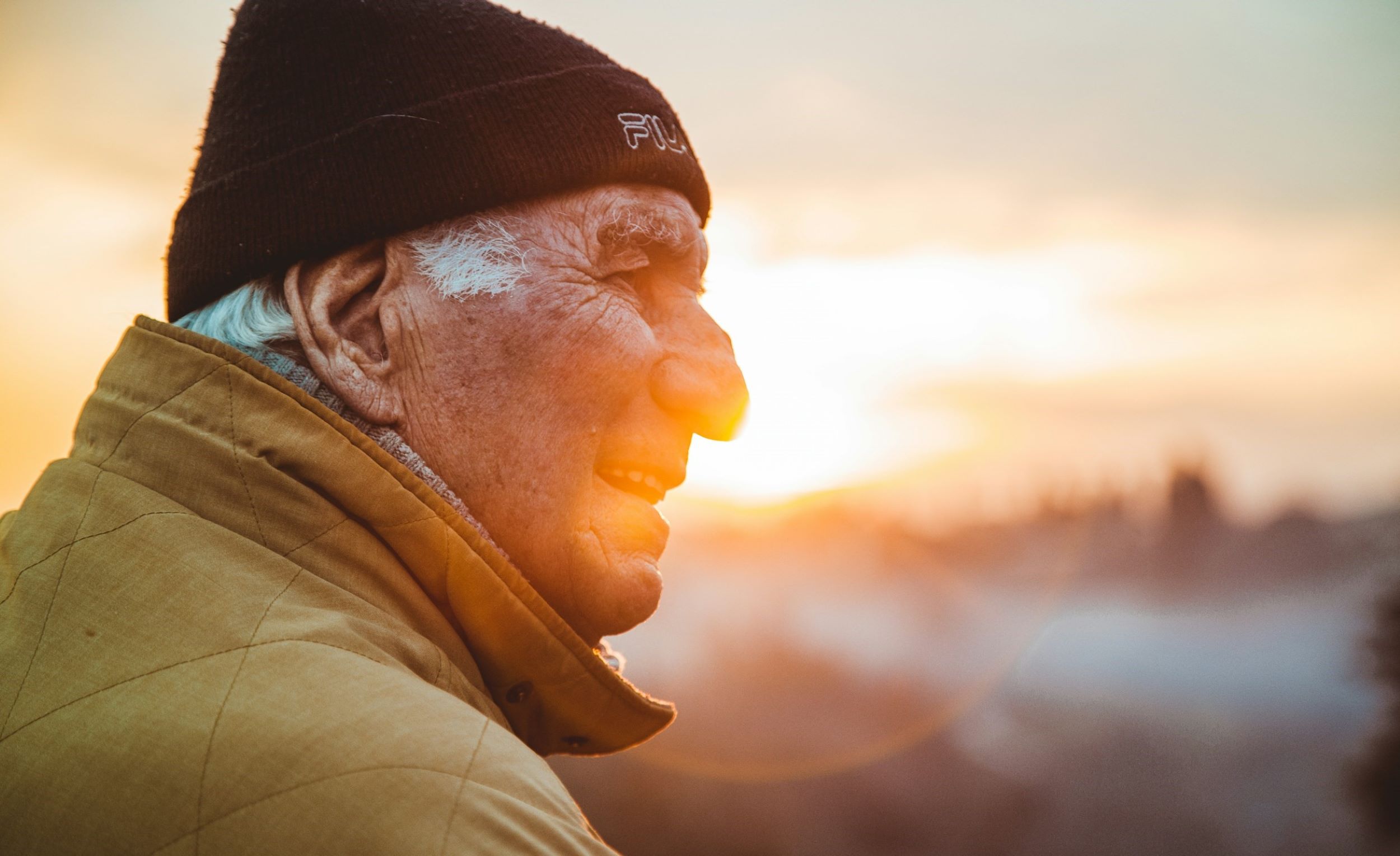 An elderly man smiles softly as he watches the sunrise.