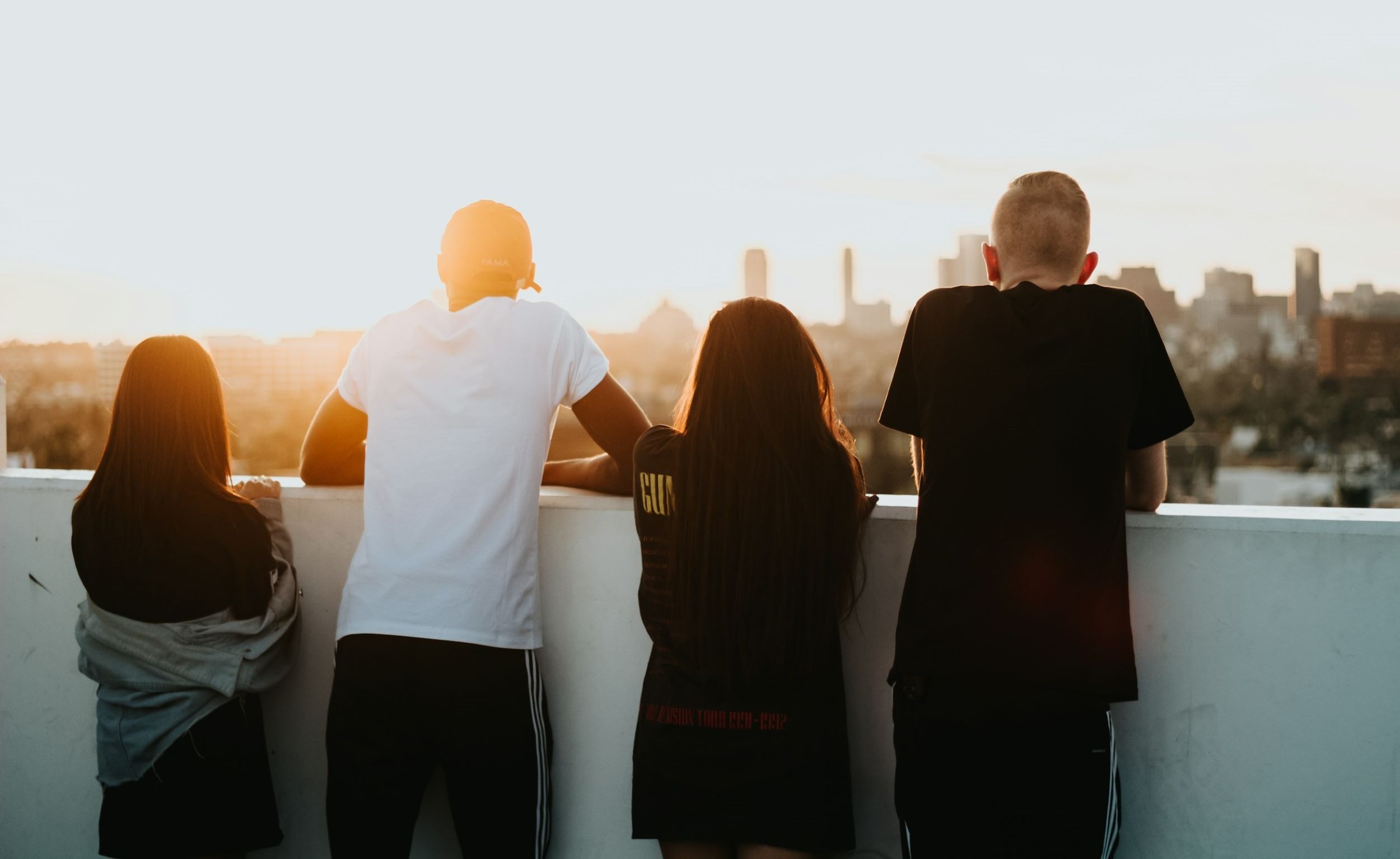 Four young people stand atop a rooftop, gazing out as the city skyline stretches before them.