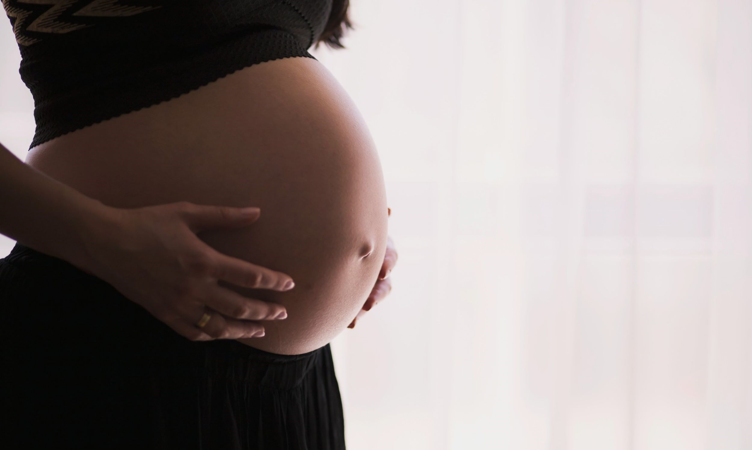 A pregnant woman clutches her stomach in front of a white backdrop.